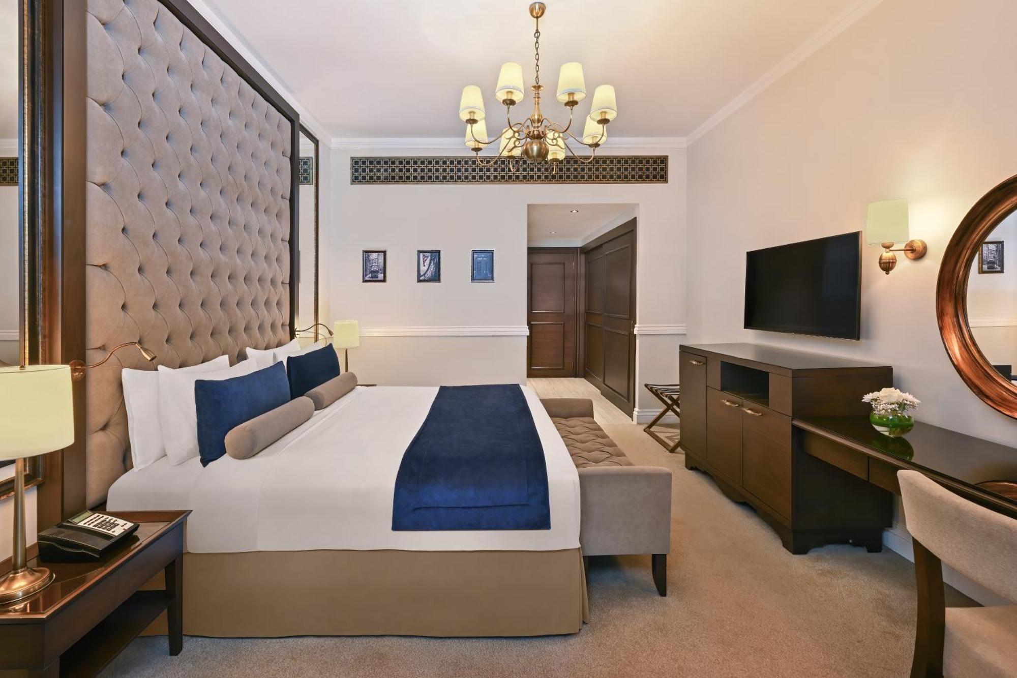 Dukes The Palm, A Royal Hideaway Hotel Дубай Екстер'єр фото The image shows a hotel room featuring a large, neatly arranged bed with decorative pillows. The headboard is tufted and upholstered in a beige fabric. There is a small sofa or bench at the foot of the bed in a contrasting color. The room is well-lit